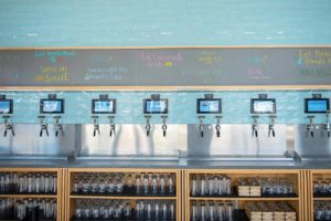 A colorful self-pour tap wall showing different drink types and glasses